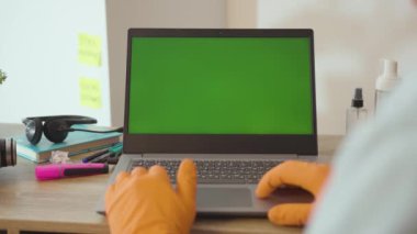 Elle çekilen adam koruyucu eldiven giyer yeşil ekran COVID-19 izolasyon pandemik koronavirüsü olan dizüstü bilgisayar kullanır evde internet iş yerinde yavaş çekim salgını olur.
