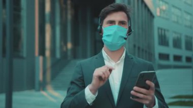 Yüz işadamı maske takıyor. Telefon ve kulaklık kullanıyor. Virüs koruması dışında konuşuyor.