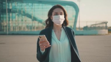 Takım elbiseli güzel beyaz bir kadın. Yüz maskesi takıyor. Akıllı telefon kullanıyor. Sağlık hizmetleri. Salgın 2020.