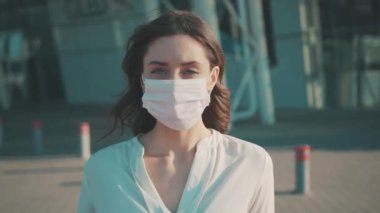 Salgın Covid-19. Güzel esmer, beyaz bir kızın portresi. Tıbbi maskesini çıkarıyor. Havaalanının dışında ciddi görünüyor. Sağlık hizmeti, yüz koruma. Karantina.