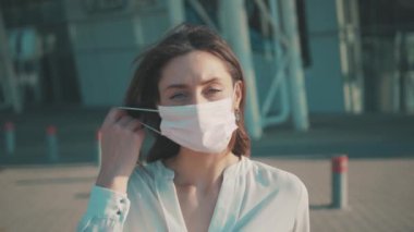 Salgın. Coronavirus. Beyaz gömlekli güzel esmer kadın temiz havayı soluyabilmek için cerrahi maskesini çıkarıyor. Şehir manzarası. Sağlık, virüs önleme.