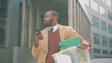 Afrikalı Amerikalı bir adam telefon kulübesinde bir kutu kişisel eşya kullanıyor. Coronavirus krizi yüzünden işten atıldı. İşsizlik ekonomisi ağır çekimde.