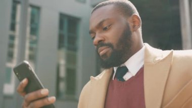 Yüzünüzü kapatın. Ciddi Afro-Amerikalı genç adam telefon kullanıyor. Gün batımında caddede duruyor.