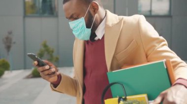 Afrikalı Amerikalı bir adam telefon kulübesinde bir kutu kişisel eşya kullanıyor. Coronavirus krizi yüzünden işten atıldı. İşsizlik ekonomisi ağır çekimde.
