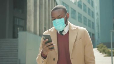 Yüz maskesi takan Afro-Amerikalı adam sokak koronavirüsüne telefon kullanıyor güvenlik önlemi pandemik salgın salgını tıbbi maske yavaş çekim