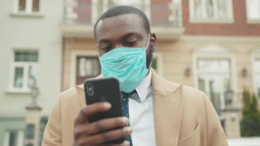 Yüz maskesi takan Afrikalı Amerikalı adam sokak koronavirüsüne telefon kullanıyor. Güvenlik önlemi, salgın salgını, tıbbi maske, yavaş çekim.