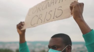 Kızgın, Afrikalı, işsiz ve işsiz bir adam Coronavirus Krizi afişini dağın tepesinde bağırarak gösteriyor. Salgın. Sarışın işsizlik.