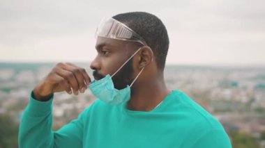 Profil yakışıklı Afro-Amerikalı doktor cerrahi maske takıyor ve koruyucu gözlük takıyor. Virüs önlemeye hazır. Coronavirus. Salgın. Sağlık hizmetleri.