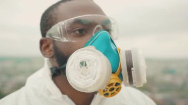 Ciddi bir siyah bilimadamı tüm vücudunu koruyor. Solunum maskesini çıkarıyor. Şehir merkezine doğru bakıyor. Açık hava portresi. Salgın. Karantina sona erdi. Özgürlük kavramı.