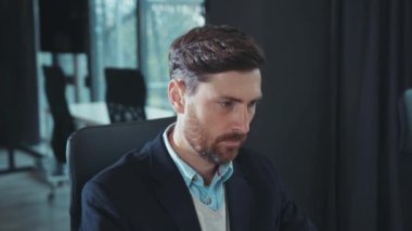 Yorgun genç iş adamı bilgisayar kullanıyor. Modern ofis teknolojisi portresi şirketinin ağır çekimde kapanış yaptığı için baş ağrısı çekiyor.