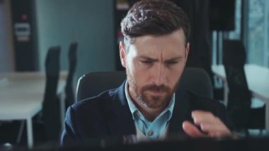 Yorgun genç işadamı bilgisayar kullanıyor. Modern ofis teknolojisi portresi şirketinin ağır çekim kapanışında baş ağrısı hissediyor.