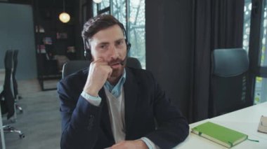 Yakışıklı adam iş için kulaklık kullanıyor. Kameraya bakın. Modern ofis programcısına gülümsüyor.