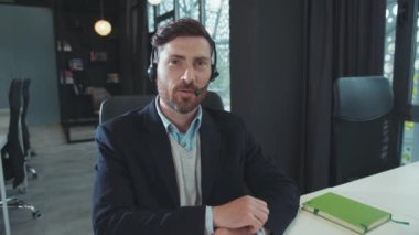 Portre yakışıklı adam iş için kulaklık kullanıyor. Kameraya bakın. Modern ofis programcısına gülümsüyor.