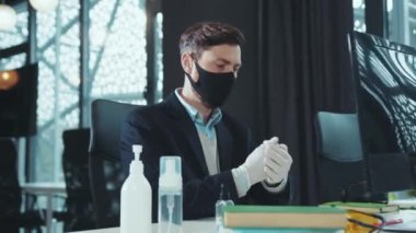 Ciddi bir adam maske takıyor bilgisayar karantinasında çalışırken antiseptikle ellerini dezenfekte ediyor bilgisayar hijyenik ofis çalışanı salgın hijyenik dezenfeksiyon salgını klavyesi üzerinde çalışıyor.