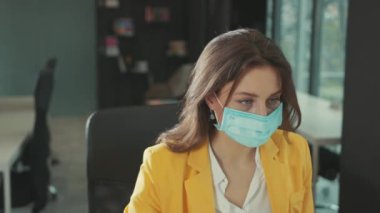 Koruyucu yüz maskesi takan sağlıklı beyaz iş kadını beyaz cerrahi eldivenler ofis bilgisayarında çalışmaya devam eden temiz havayı soluyor..