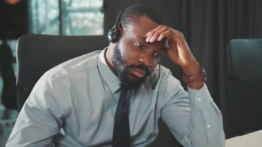 Üzgün Afro-Amerikalı yakışıklı erkek modern ofis programcılarında bilgisayar ve kulaklık kullanıyor. Monitör ekranına ciddi ciddi bakıyor ve mühendislik problemlerini yavaş çekimde çözüyor.