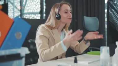 Neşeli sarışın genç iş kadını arkadaşlarıyla sohbet ediyor. İnternetteki görüntülü sohbet bilgisayarında. Ofiste el kol hareketi yapıyor ve gülümsüyor..