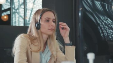 Kulaklıklı, uykulu, sıkkın, genç, sarışın bir kadın, müşterilerine Dekstop bilgisayarındaki görüntülü sohbet konuşmalarıyla uyandı. Sıkıcı bir iş ve meslek..