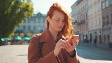 Çekici kızıl saçlı kadın. Akıllı telefon kullanıyor. Negatif içerik kullanıyor. Kötü haberler okuyor..
