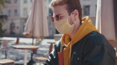 Maskeli genç çekici bir adam portatif dizüstü bilgisayarla iş projesi üzerinde çalışıyor. Terrace Cafe City Center 'ın önünde oturuyor..