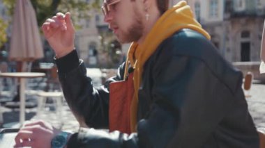 Genç konsantre olmuş serbest çalışan portatif dizüstü bilgisayarla uzaktan kumandayı bitiriyor güzel şehir merkezindeki kafenin terasında kameraya neşeyle gülümsüyor..