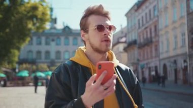 Şık giyinen yakışıklı beyaz adam sokak şehir merkezinde yürüyor akıllı telefon sosyal medyasında kitap okuyor şok edici içeriği çok üzülüyor. Kötü haber, olumsuz..