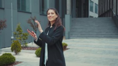 Dışarıda dans eden ve akıllı telefon tuşları yazan neşeli, mutlu, genç, güzel ofis kadını. Kullanıcı arayüzü ile animasyon için. Sosyal medya etkileyicisi. Geri bildirim.