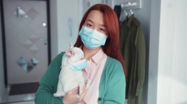 Çekici Asyalı genç bir kadın şirin Chihuahua köpeğini tutuyor, ikisi de koruyucu maskeler takıyor ve evde karantinada kalıyor. Coronavirus. Sağlık hizmetleri.