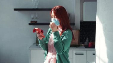Mutlu, güzel, Asyalı genç bir kadın, erkek arkadaşıyla akıllı telefon sohbeti yapıyor. Mutfakta büyük bir sevinçle mesajlaşıyor. Evde kal. Sosyal uzaklık. Çevrimiçi iletişim.