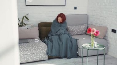 Sıcak oturma odasında battaniyenin altında soğuktan titreyen Asyalı hasta genç kadın. Sağlık hizmetleri. Grip belirtileri. Coronavirus. Karantina.