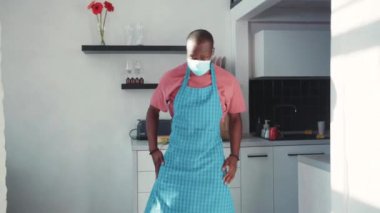 Komik Afro-Amerikalı önlüklü genç aşçı mutfakta dans ederken müziğin tadını çıkarıyor. Evde yalnızım. Karantinada iyi eğlenceler. Sosyal uzaklık.