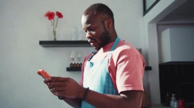 Kaçak Afro-Amerikalı adam internette harika haberler okuyor ve anında başarı sayesinde gülümsüyor. Mutfakta yemek önlüğü giymiş mutlu, şaşırmış adam..