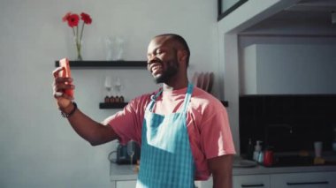 Video görüşmesi için akıllı telefonu kullanan, arkadaşlarıyla internetten sohbet eden, kendi mutfağında kalan yakışıklı bir zenci. Bağlantı. İletişim kuran insanlar.