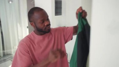 Siyah yakışıklı adam aynanın önünde işe gitmek için giyiniyor. Ceket giyen genç bir Afrikalı iş için dizüstü bilgisayarla evden ayrılıyor. Dışarı çıkıyorum. Yaşam biçimi.