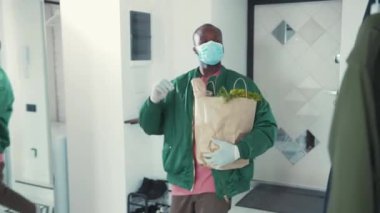 Afro-Amerikalı adam eve yiyecek paketiyle giriyor, cerrahi maskesini çıkarıyor. İşten eve dönen yakışıklı bir adam. Sıradan bir yaşam tarzı. Her zamanki gibi. Sağlık hizmetleri. Karantina.