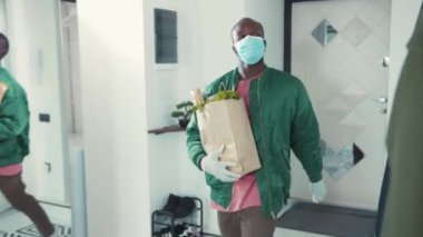 Yemek alışverişinden sonra eve dönen yakışıklı bir adam. Genç Afrikalı bir adam eve giriyor ve maskesini çıkarıyor. Karantina sırasında sağlık sigortası. Coronavirüs.