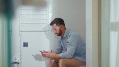 Komik mutlu iş adamı tuvalette oturup gülümseyen cep telefonu akıllı telefon internet ev tuvaletini kullanıyor.