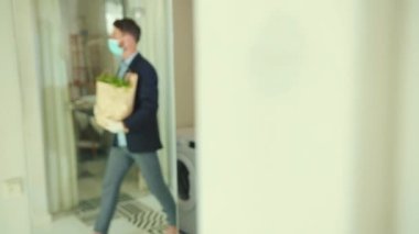 Çekici stil sahibi bir adam eve yemek alışverişinden sonra geliyor maske paketini çıkartıyor salgını koruyor karantina enfeksiyonunu karantina altına alıyor sosyal mesafeyi geri döndürüyor kendine özen gösteren virüsü yavaş yavaş geri getiriyor.