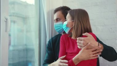 Pencere kenarında oturan güzel çift, tıbbi maske takıyor, koronavirüs takıyor, karısına sarılıyor, kocasına baskı yapıyor, depresyon penceresini kilitliyor, ağır çekimde sıkılıyor.