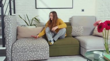 Kanepede oturmuş telefondan mesaj bekleyen komik bir kadın akıllı telefonlu bir konuşma gülüşüne bakıyor. Alet edevat kızında kalıyor. Güzel çevrimiçi çekici teknoloji.