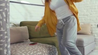 Kanepede oturmuş, telefondan mesaj bekleyen gülümseyen bir kadın akıllı telefona bakıp mutlu bir şekilde evde oturuyor güzel, çevrimiçi, alımlı, çekici teknolojiyi yavaş çekimde kapatıyor.