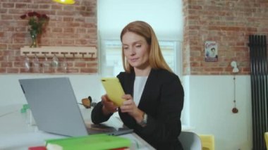 Gülümseyen çekici genç iş kadını akıllı telefondan konuşuyor ev ofisteki dizüstü bilgisayarı kullanıyor başarılı bağlantı teknolojisi iletişimi yavaş çekim internet