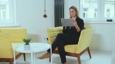 Kadın, evdeki iş kadını konseptindeki tablet bilgisayarını kullanarak kanepeye oturur. Dokunmatik ekran güzel, modern, yavaş çekim yakın çekim.