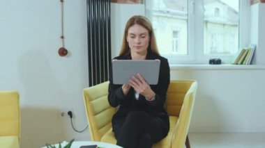 Mutlu kadın evdeki iş kadını konseptinde tablet bilgisayar kullanarak kanepeye oturur. Dokunmatik ekran güzel, yavaş çekimde yakın çekim.