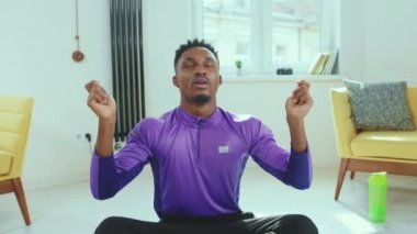 Afrika kökenli Amerikalı adam Lotus 'ta oturuyor. İnternette dizüstü bilgisayarın yanında oturuyor. Yoga sağlık teknolojisi yavaş çekim çalışmasından sonra internetten gözlerini kapatıp meditasyon yapıyor.