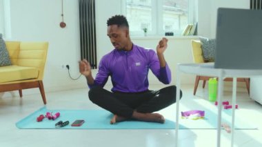 Afrika kökenli Amerikalı bir adam Lotus 'ta dizüstü bilgisayarın yanında oturmuş yerde tek başına meditasyon yapıyor. Telefon görüşmesi, sağlık teknolojisi yavaş çekim çalışmasından sonra internetten yoga yaparken kesiliyor.