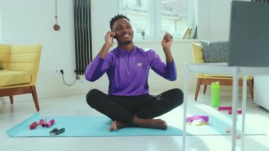 Yavaş çekim Afrikalı Amerikalı adam evde dizüstü bilgisayarın yanında oturmuş yerde tek başına meditasyon yapıyor telefon görüşmesi sağlık teknolojisi eğitiminden sonra internetten yoga yaparken kesiliyor.