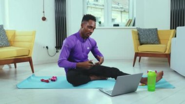 Çekici Afrikalı Amerikalı adam çevrimiçi konuşuyor ve karantina antrenörü spor salonu spor salonu spor salonu ağır çekim egzersiz sırasında dizüstü bilgisayar ekipmanları kullanıyor.