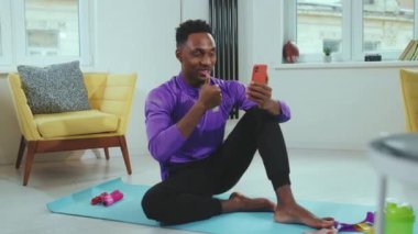 Eğitimden sonra mutlu Afrikalı Amerikalı genç adam, video çağrısından sonra gülümse. Işık odasına gidip akıllı telefon sohbetini ara. Bağlantı ağları yavaş çekim.