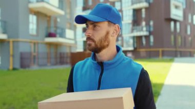 Yakışıklı, genç, mutlu, karton kutu taşıyan teslimatçı. Sokak alışveriş paketine bak. Postacı ağır çekimde.